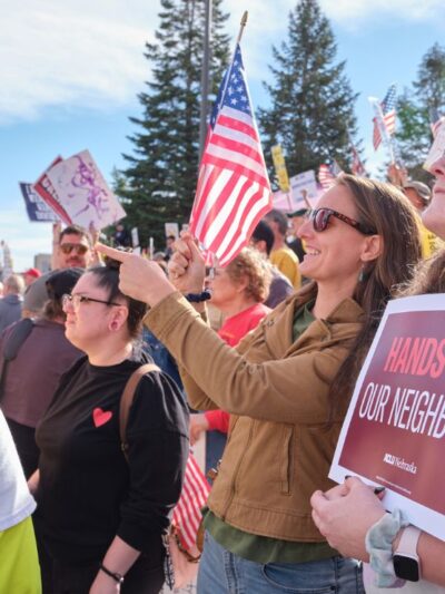 Nebraskans gather at a No Kings protest in Lincoln, NE in October of 2025. One holds an ACLU sign reading "Hands off our neighbors."