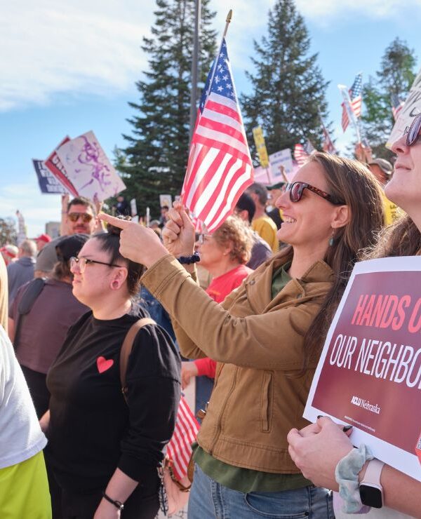Nebraskans gather at a No Kings protest in Lincoln, NE in October of 2025. One holds an ACLU sign reading "Hands off our neighbors."