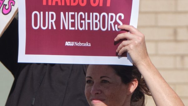 A protester holds a sign reading Hands off our neighbors.