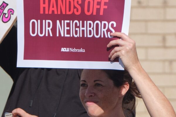 A protester holds a sign reading Hands off our neighbors.