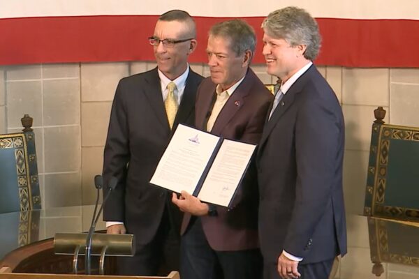 DHHS Secretary Corsi, Gov. Pillen, and AG Hilgers smile next to Pillen's EO, which is intended to pull funding for reproductive health care services.