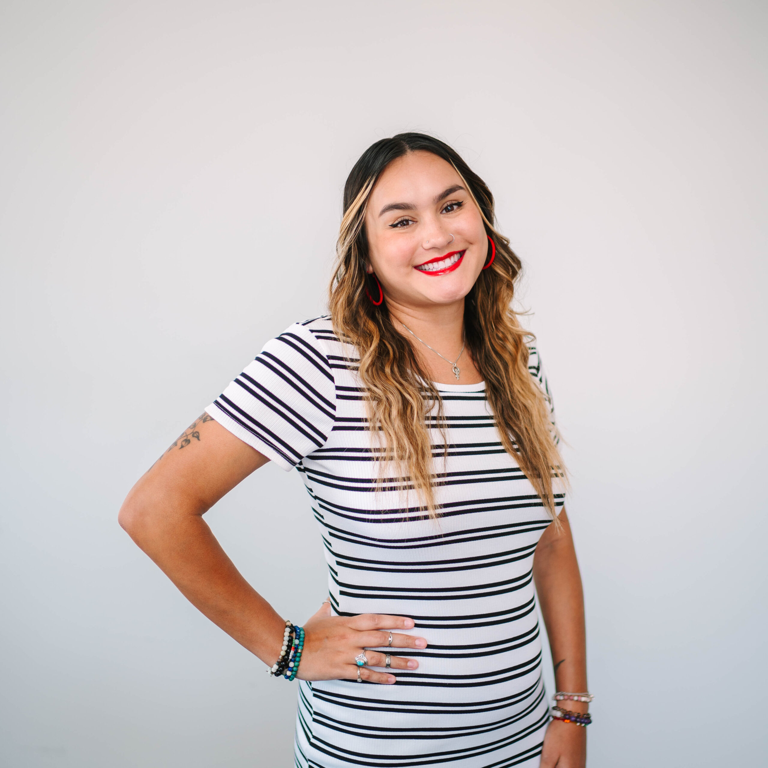 Adairah Thapa, standing in front of a white background with a black and white stripped dress