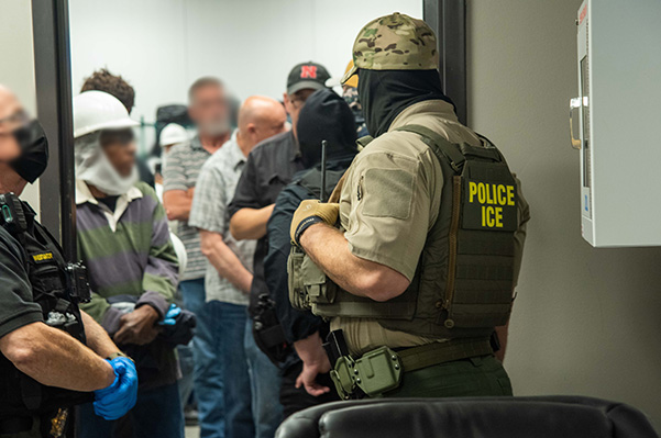 Image shows masked ICE agent with his back to the camera with the words "POLICE ICE" in yellow.