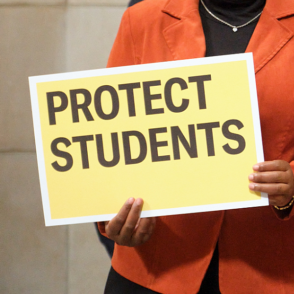 A press conference attendee holds a sign reading Protect Students at the Nebraska State Capitol.