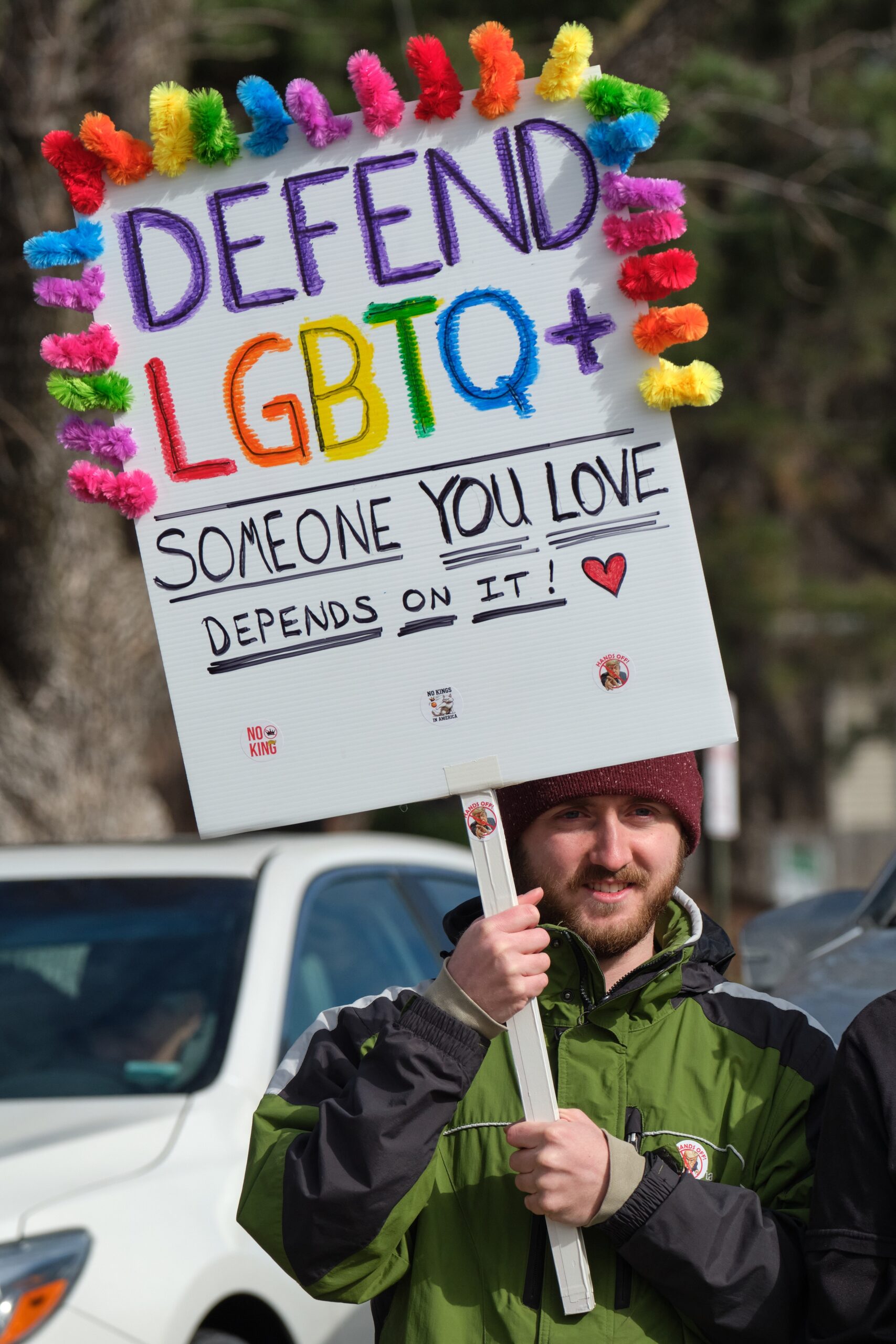 A protester holds a sign reading "Defend LGBTQ+ Someone you love depends on it."