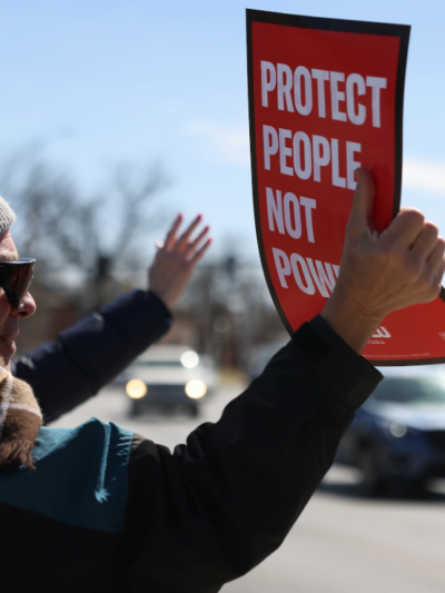 A protester holds an ACLU sign reading "protect people not power"