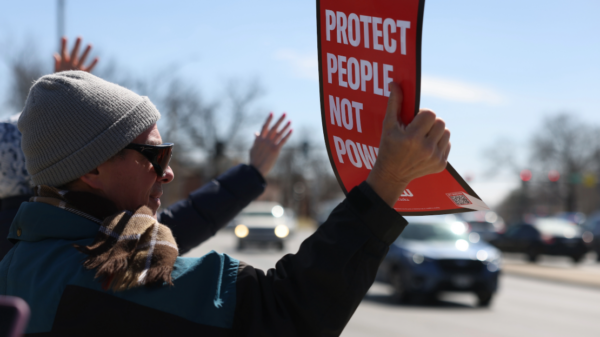 A protester holds an ACLU sign reading "protect people not power"