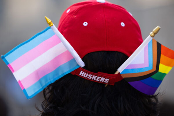 A photo shows someone with a pride and trans pride flag in their Husker hat. Photo by Rebecca Gratz.