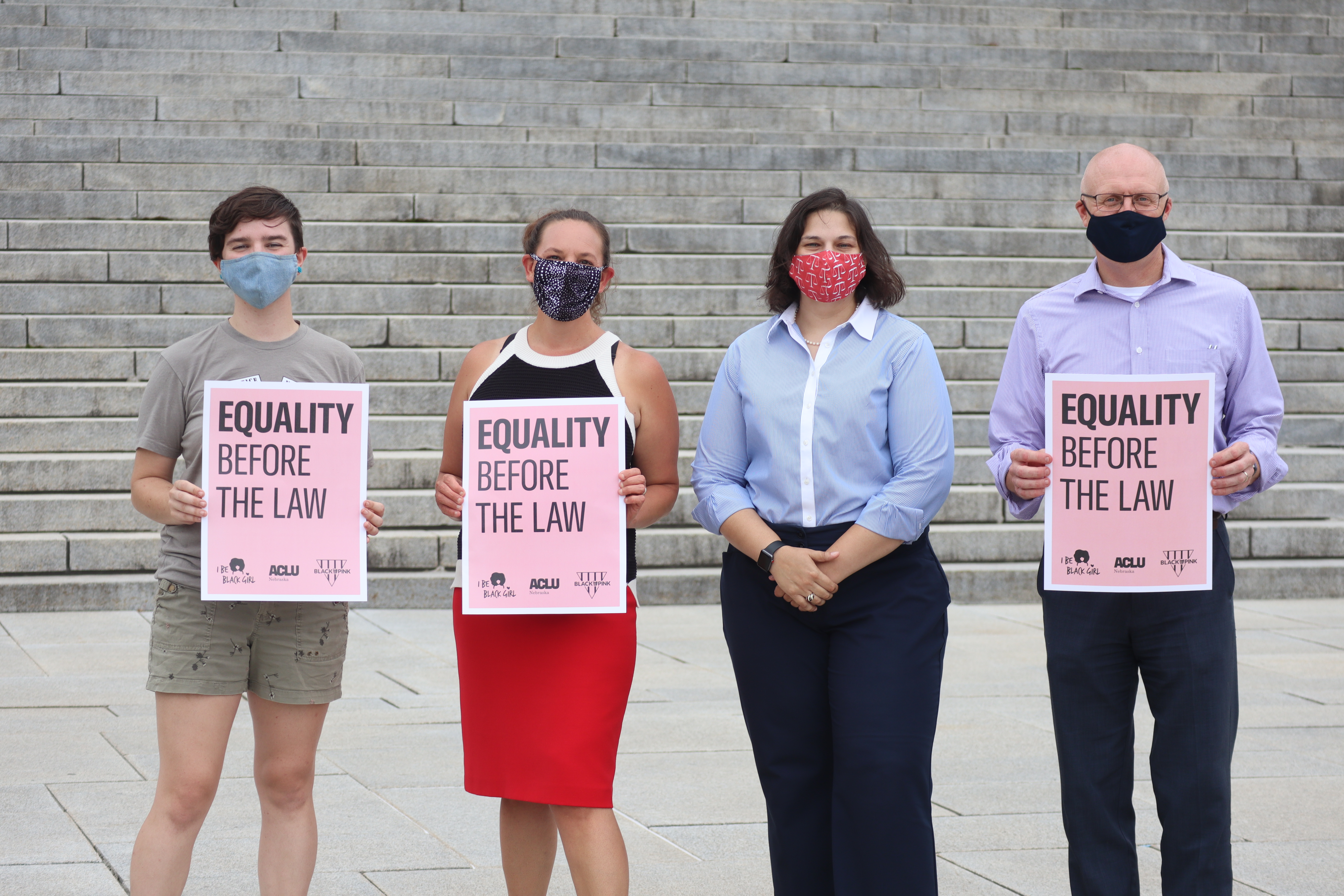 Four ACLU staff members stand outside the Nebraska State Capitol, three of whom are holding signs reading "Equality Before the Law."