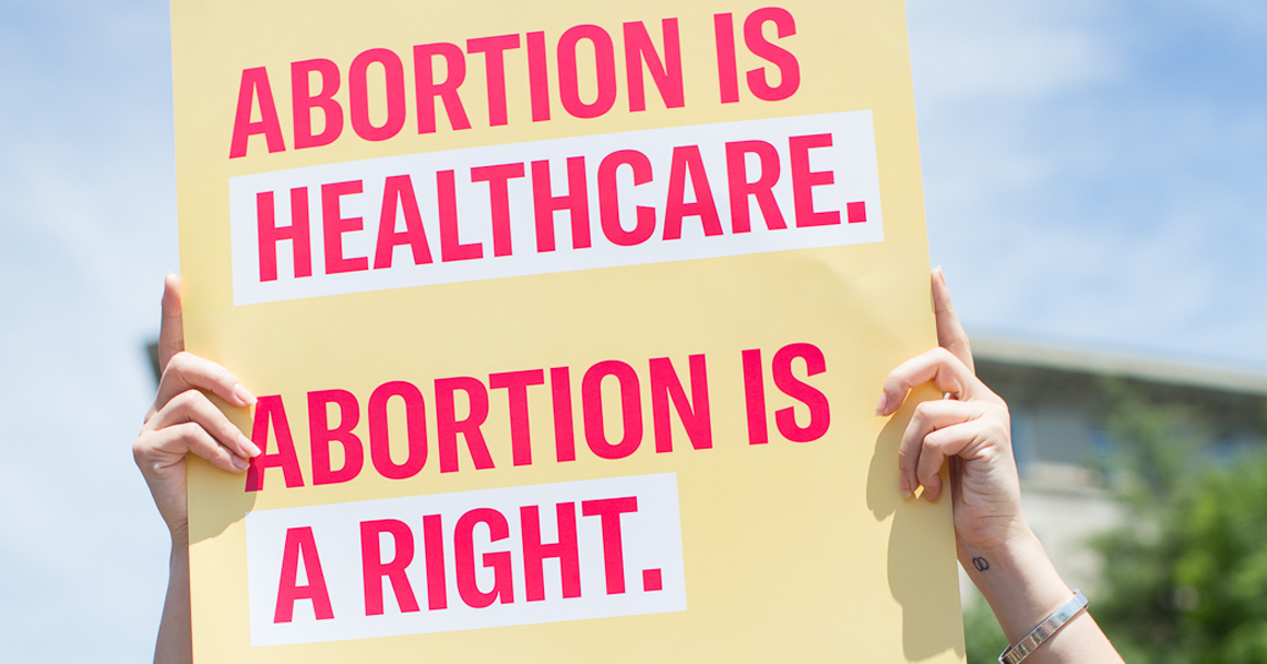 A photograph shows two hands holding a sign reading "Abortion is healthcare. Abortion is a right."