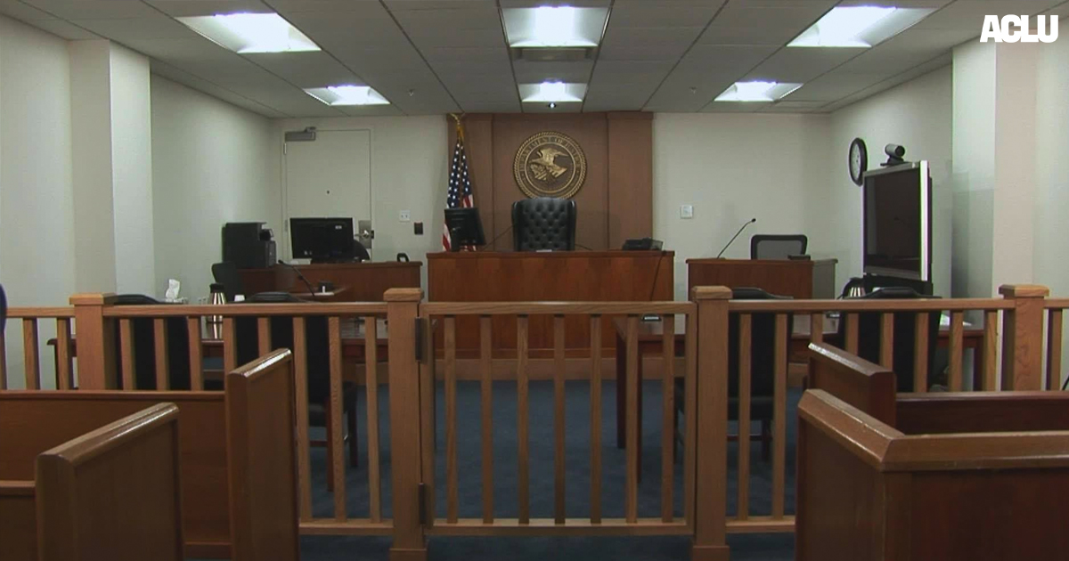 An image of an immigration court shows dark wood seating, a government seal, and panel lighting.