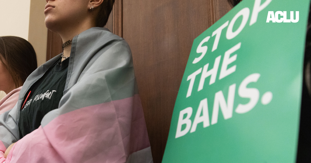 A Nebraskan wrapped in the trans flag listens to testimony during a committee hearing for the near-total abortion ban.
