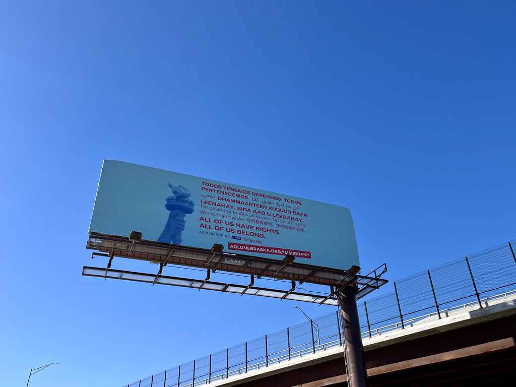 A light blue billboard shows the Statue of Liberty's torch next to translated text, all reading "All of us have rights. All of us belong."