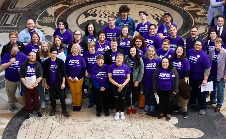 Photo taken from above and angled down. Nebrakans wearing purple shirts pose in the Nebraska Capitol Rotunda