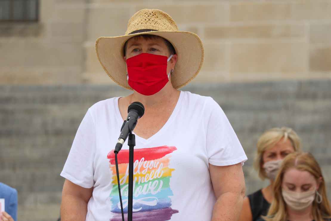 Abbi speaks at a rally outside the Nebraska State Capitol wearing a rainbow shirt that says All You Need is Love.