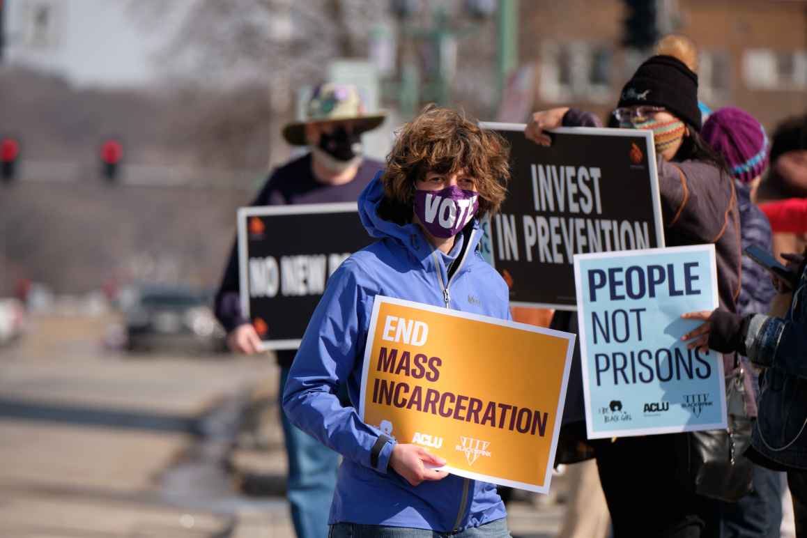 Protesters stand alongside a Lincoln street, holding signs that read "End mass incarceration" and "People not prisons."