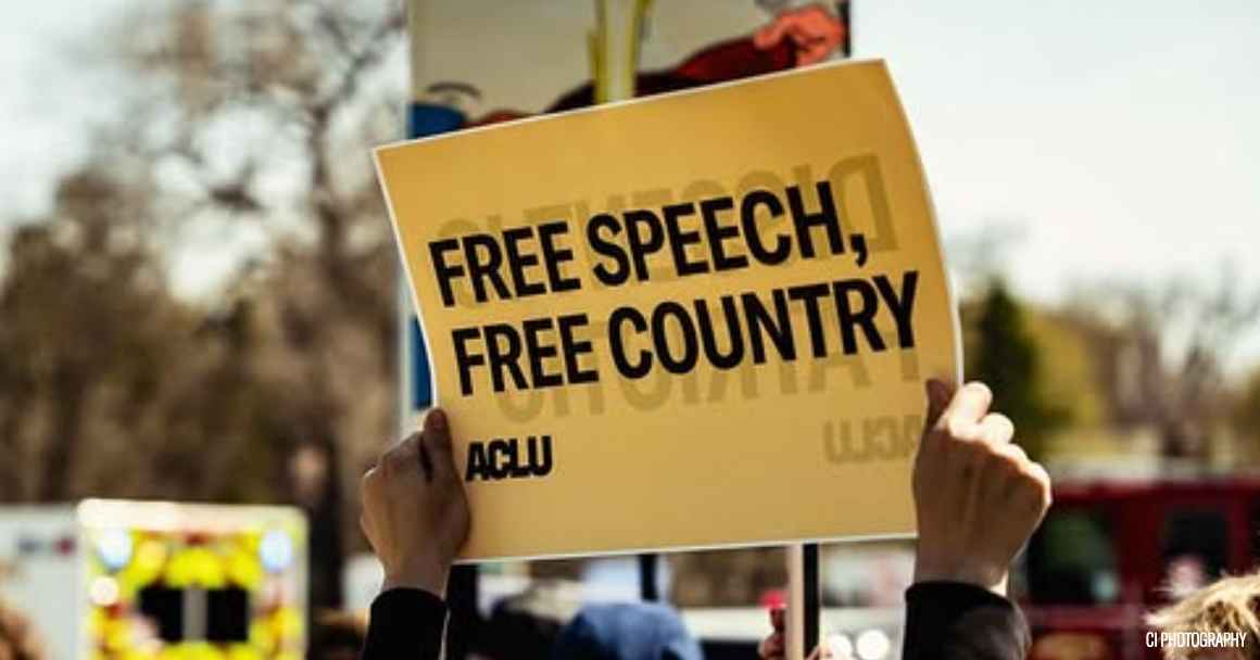A rally attendee in Omaha holds an ACLU sign reading "FREE SPEECH, FREE COUNTRY."