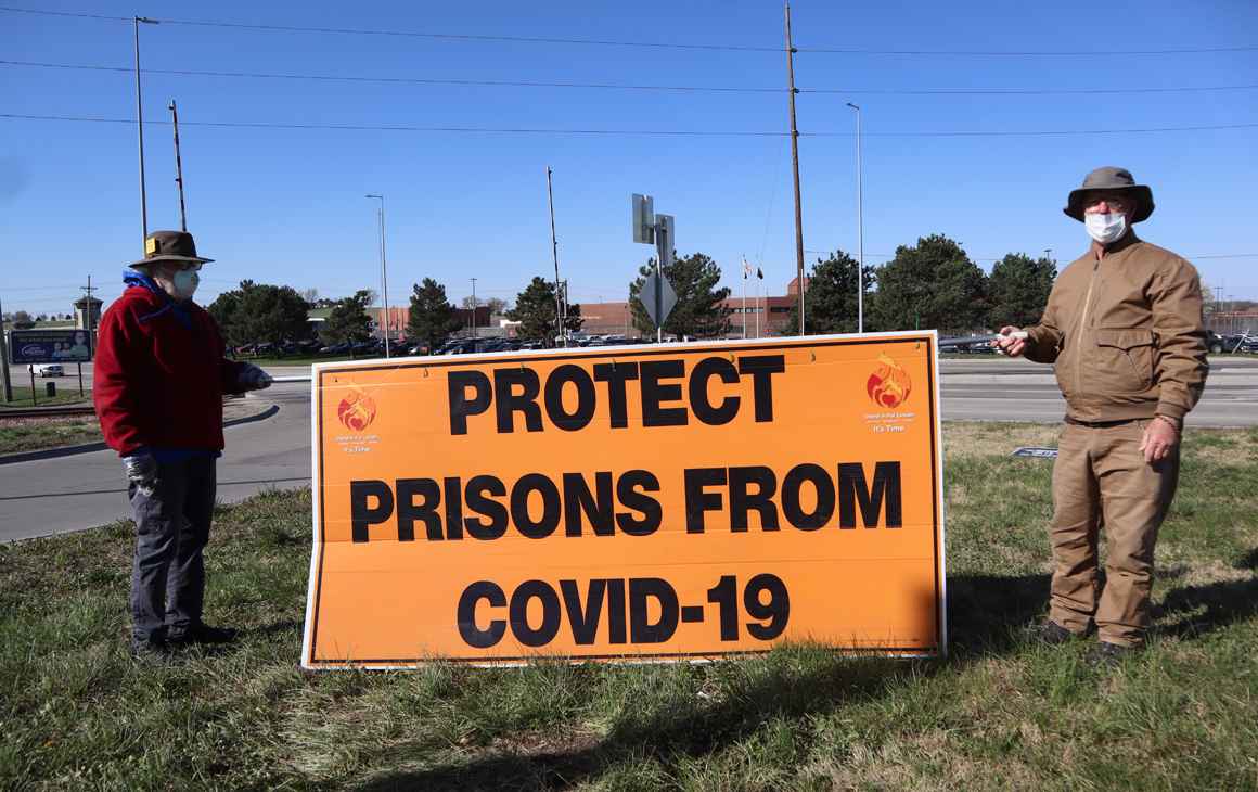 Rex Walton and Paul Feilmann hold a sign reading "Protect prisons from COVID-19" outside of the Nebraska State Penitentiary.