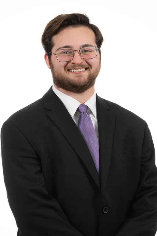 Image of Grant Friedman, a smiling man with white skin and brown short hair who is wearing glasses, a black suit, and a purple tie.