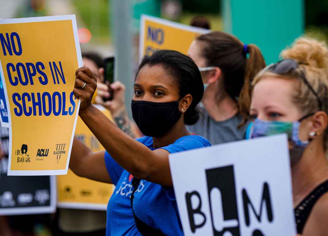 A protester holds a sign reading "No Cops in Schools."