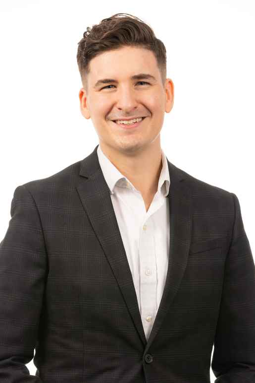 This image of Sam Petto shows a smiling man with white skin and dark wavy hair, wearing a white collared shirt and black blazer.