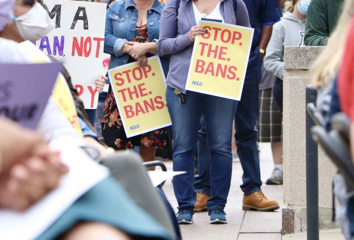 Attendees hold signs at an Omaha reproductive rights rally, reading "Stop. The. Bans."