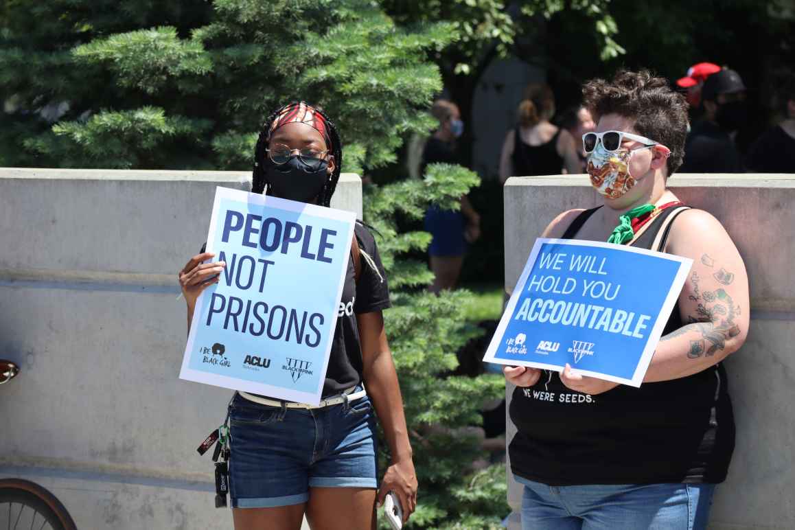 Protesters hold signs reading "People not Prisons" and "We Will Hold You Accountable"