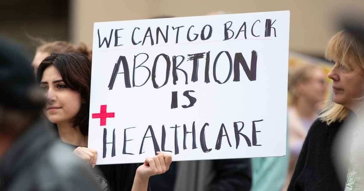 A woman at a rally holds a sign reading "We can't go back. Abortion is health care."