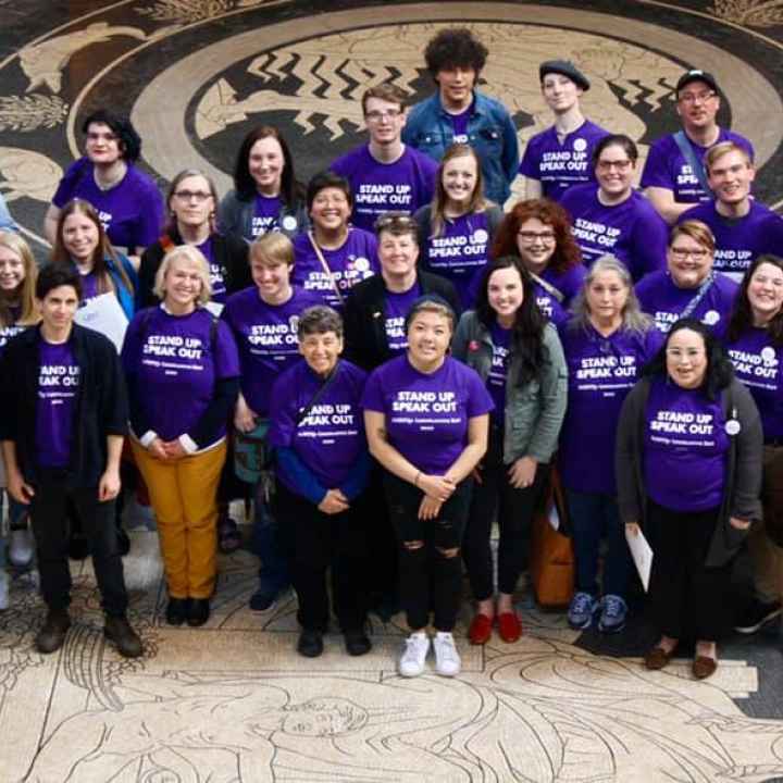Photo taken from above and angled down. Nebrakans wearing purple shirts pose in the Nebraska Capitol Rotunda