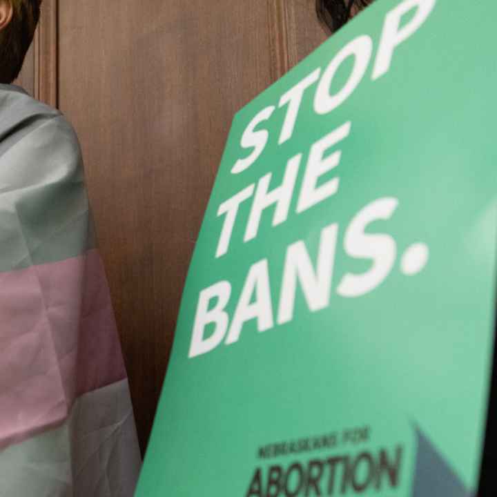 A Nebraskan wrapped in the trans flag listens to testimony during a committee hearing for the near-total abortion ban.