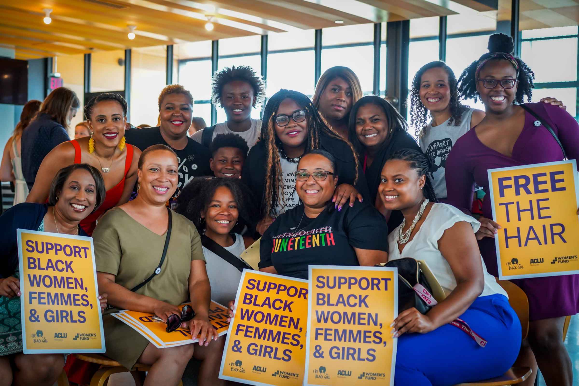 A group of women pose for a photo holding signs reading "Support Black Women, Femmes & Girls"