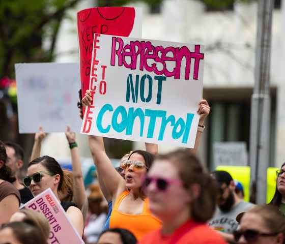 A Nebraskan holds a sign reading "Elected to Represent. Not Control."